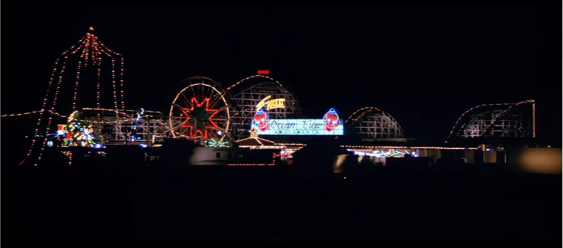 Establishing shot of Oceanview Park at night, all the rides are lit up with lights